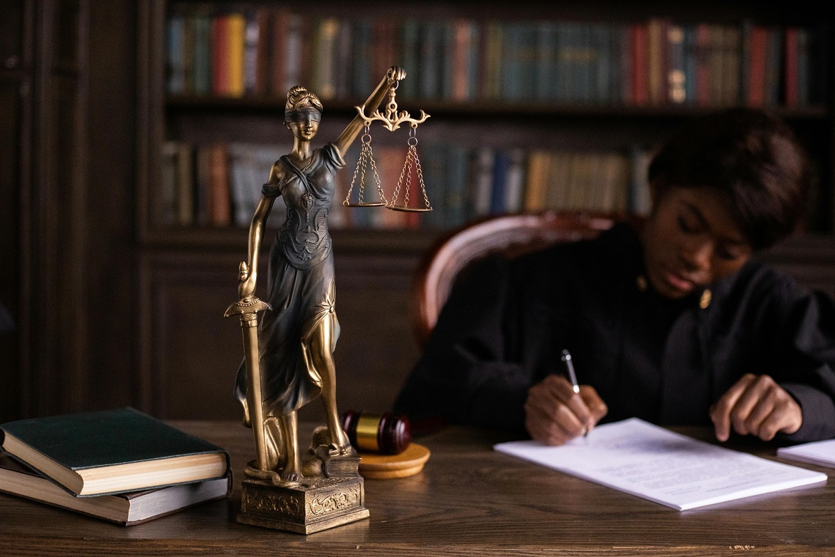 lady justice figurine with a judge writing in the background